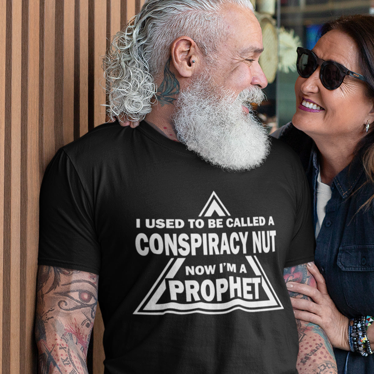 Man wearing a black t-shirt with text standing next to a woman. This conspiracy theorist t-shirt design is for anyone who used to get funny looks for their alternative view, but now gets greeted with nods of understanding as your earlier rantings come true. Made from 100% organic ring-spun cotton, this conspiracy theorist t-shirt is unisex, high-quality, super comfy, and best of all, eco-friendly.