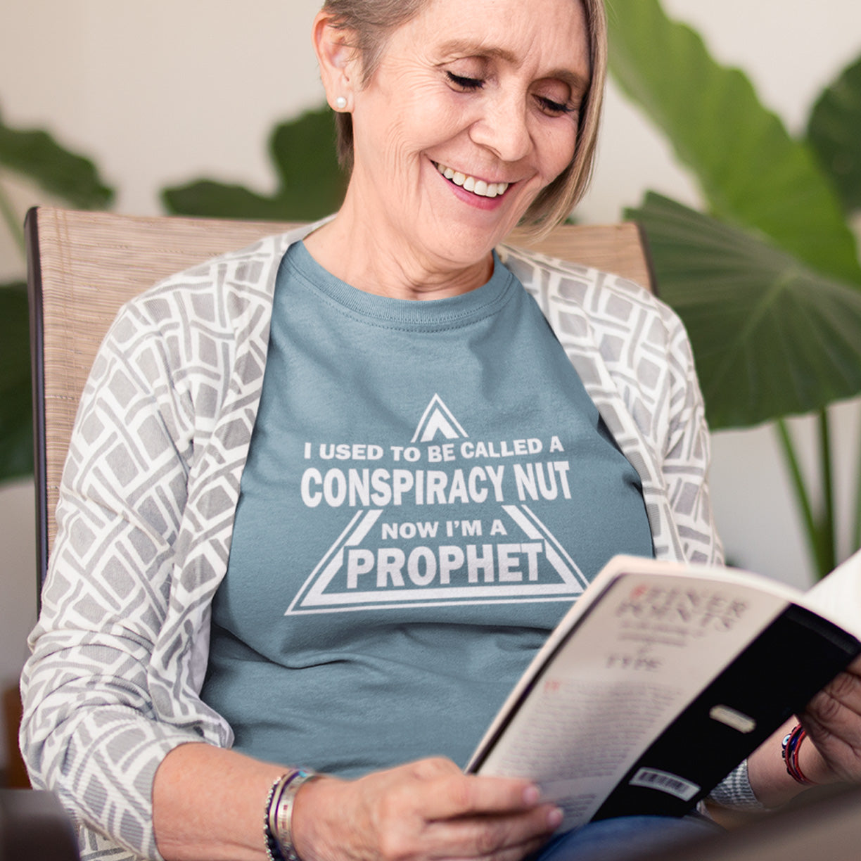 Woman wearing a shirt with text reading 'I used to be called a conspiracy nut now I'm a prophet' while reading a book. This conspiracy theorist t-shirt design is for anyone who used to get funny looks for their alternative view, but now gets greeted with nods of understanding as your earlier rantings come true. Made from 100% organic ring-spun cotton, this conspiracy theorist t-shirt is unisex, high-quality, super comfy, and best of all, eco-friendly.