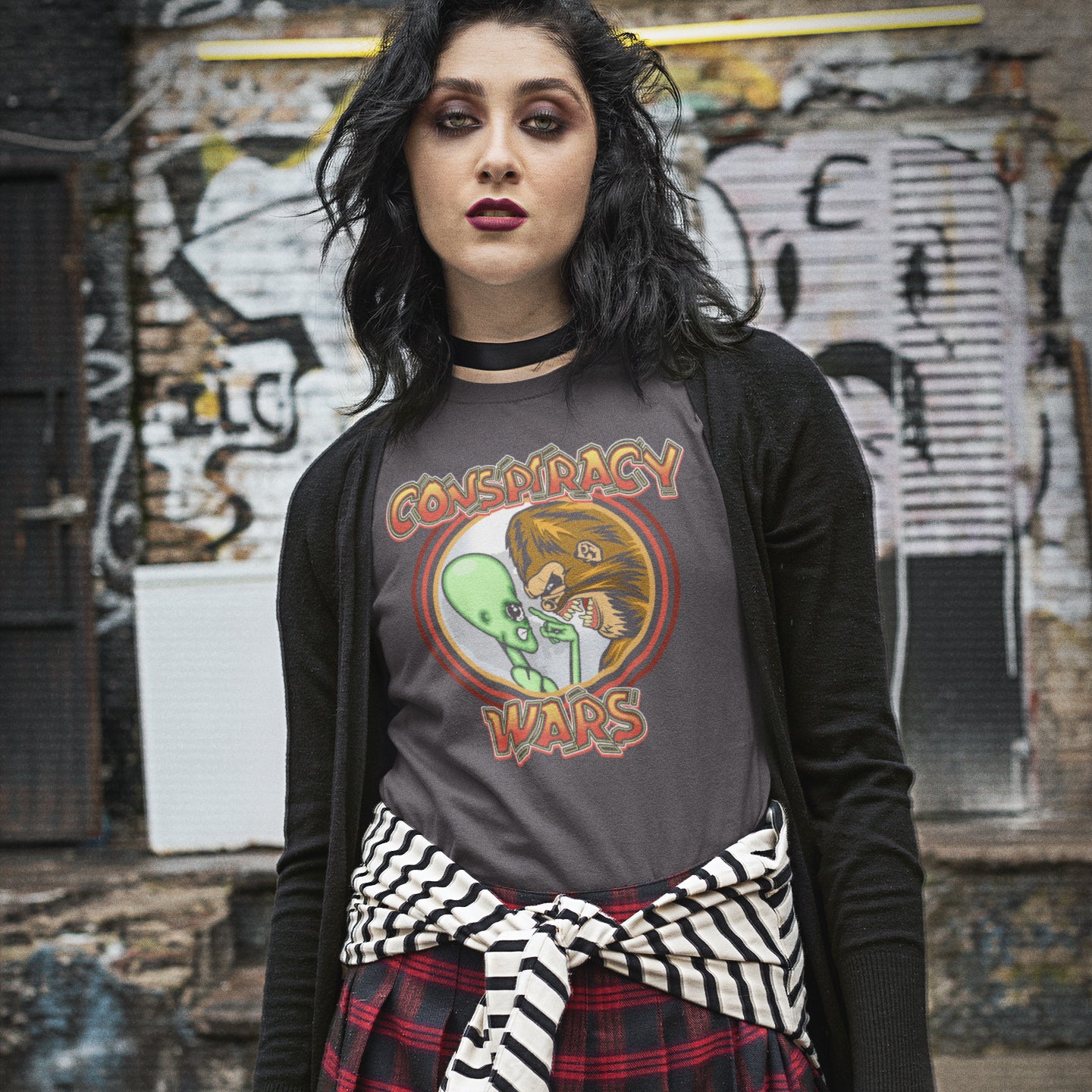 Person wearing a t-shirt with 'Conspiracy Wars' design in front of a graffiti-covered wall. This funny conspiracy t-shirt suggests competition between the two main rivals for cover up stories. Aliens Vs Bigfoot, Kings of conspiracy face off. Made from 100% organic ring-spun cotton, this witty conspiracy theory t-shirt is unisex, high-quality, super comfy, and best of all, eco-friendly.