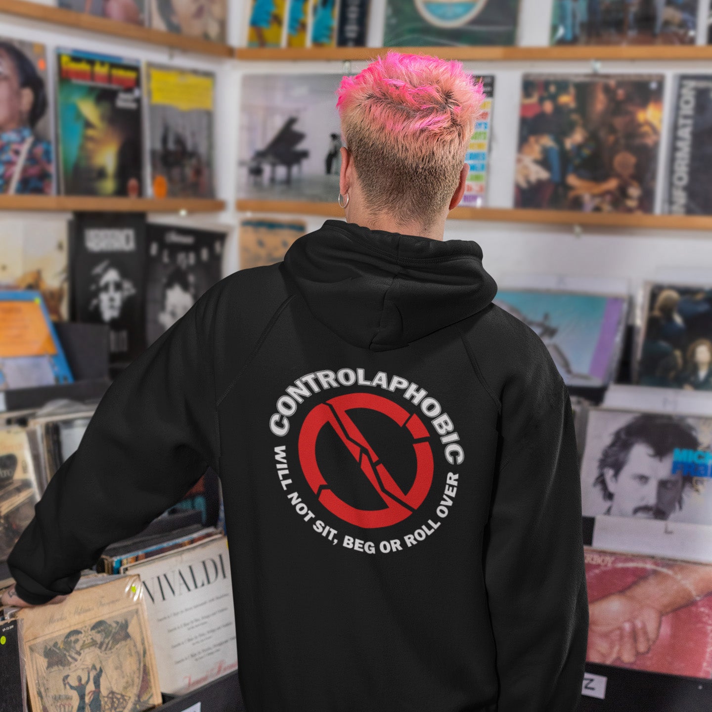 Person wearing a black hoodie with 'Controlaphobic' logo in a record store. A satirical civil rights hoodie suggesting there is a lack of freedom of choice, and too much control, in modern society. If you find yourself unable to follow commands and you're not a dog, You may have controlaphobia. Comfortable and practical. It's extra soft and has a convenient front pouch pocket. Made from organic cotton and recycled polyester, this civil rights hoodie design is a great eco-friendly choice.
