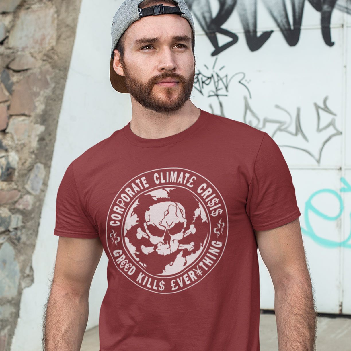Man wearing a burgundy t-shirt with a graphic design and text, standing against a graffiti-covered wall. An anti corporate t shirt encouraging social awareness and support to save our planet from corporate negligence. Make it clear you are no fool to where the climate problem blame should be placed with this original design. Made from 100% organic ring-spun cotton, this save the world t shirt is unisex, high-quality, super comfy, and best of all, eco-friendly.