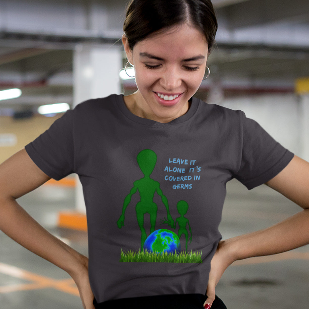 Person wearing a t-shirt with an alien graphic and text in a parking garage. A funny alien t-shirt design with a subtle overpopulation message. In the grand scheme of things, our planet and universe could just be the school project of a child from a superior race. Made from 100% organic ring-spun cotton, this witty alien t-shirt is unisex, high-quality, super comfy, and best of all, eco-friendly.