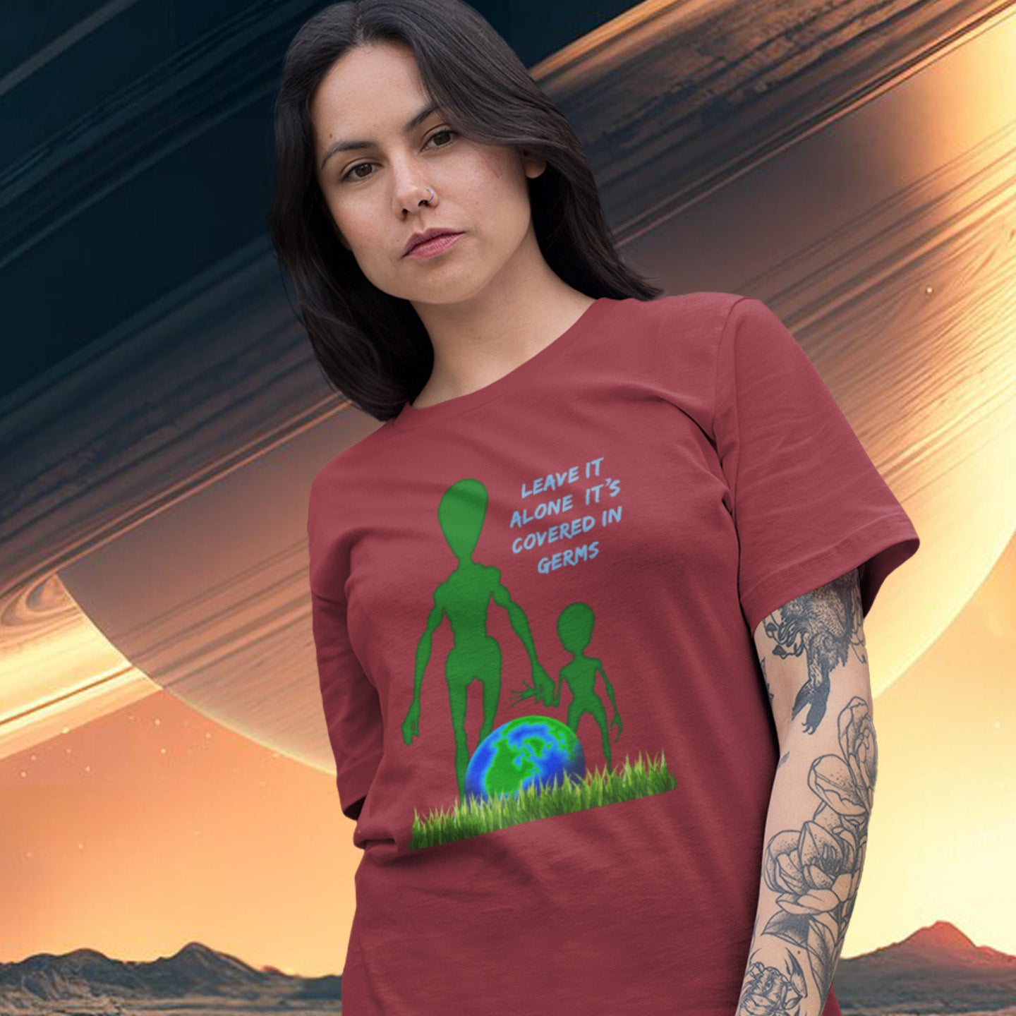 Woman wearing a burgundy t-shirt with an alien and Earth graphic and text, set against a space-themed background. A funny alien t-shirt design with a subtle overpopulation message. In the grand scheme of things, our planet and universe could just be the school project of a child from a superior race. Made from 100% organic ring-spun cotton, this witty alien t-shirt is unisex, high-quality, super comfy, and best of all, eco-friendly.