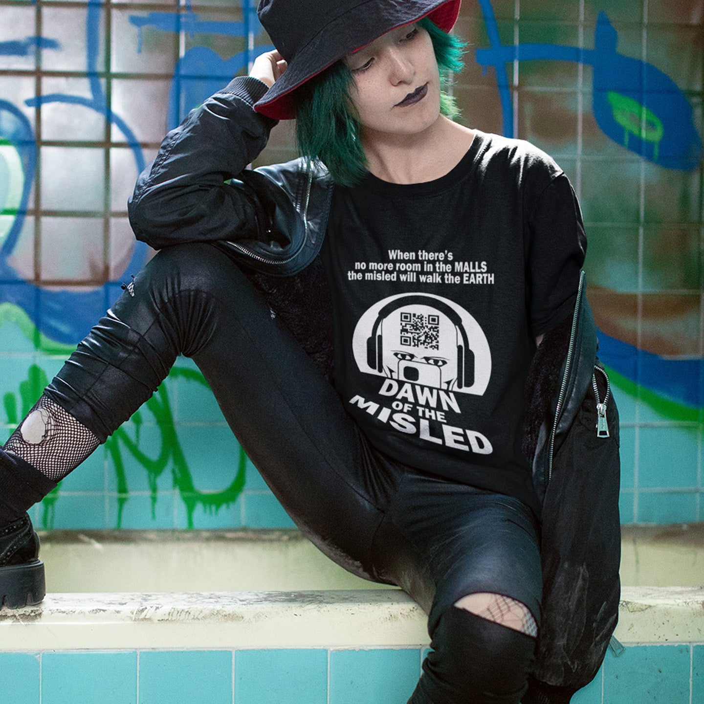 Person wearing a black sweatshirt with text and graphics, sitting against a graffiti-covered wall. A counterculture t-shirt in the theme of a famous 1970's horror movie. This satirical design highlights the modern consumer who buys what they are told to buy by social media and corporate advertising. Made from 100% organic ring-spun cotton, this underground anti-consumerism t-shirt is unisex, high-quality, super comfy, and best of all, eco-friendly.