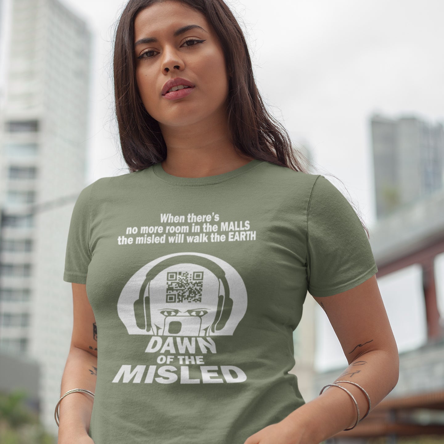 Woman wearing a green t-shirt with a graphic design and text in an urban setting. A counterculture t-shirt in the theme of a famous 1970's horror movie. This satirical design highlights the modern consumer who buys what they are told to buy by social media and corporate advertising. Made from 100% organic ring-spun cotton, this underground anti-consumerism t-shirt is unisex, high-quality, super comfy, and best of all, eco-friendly.