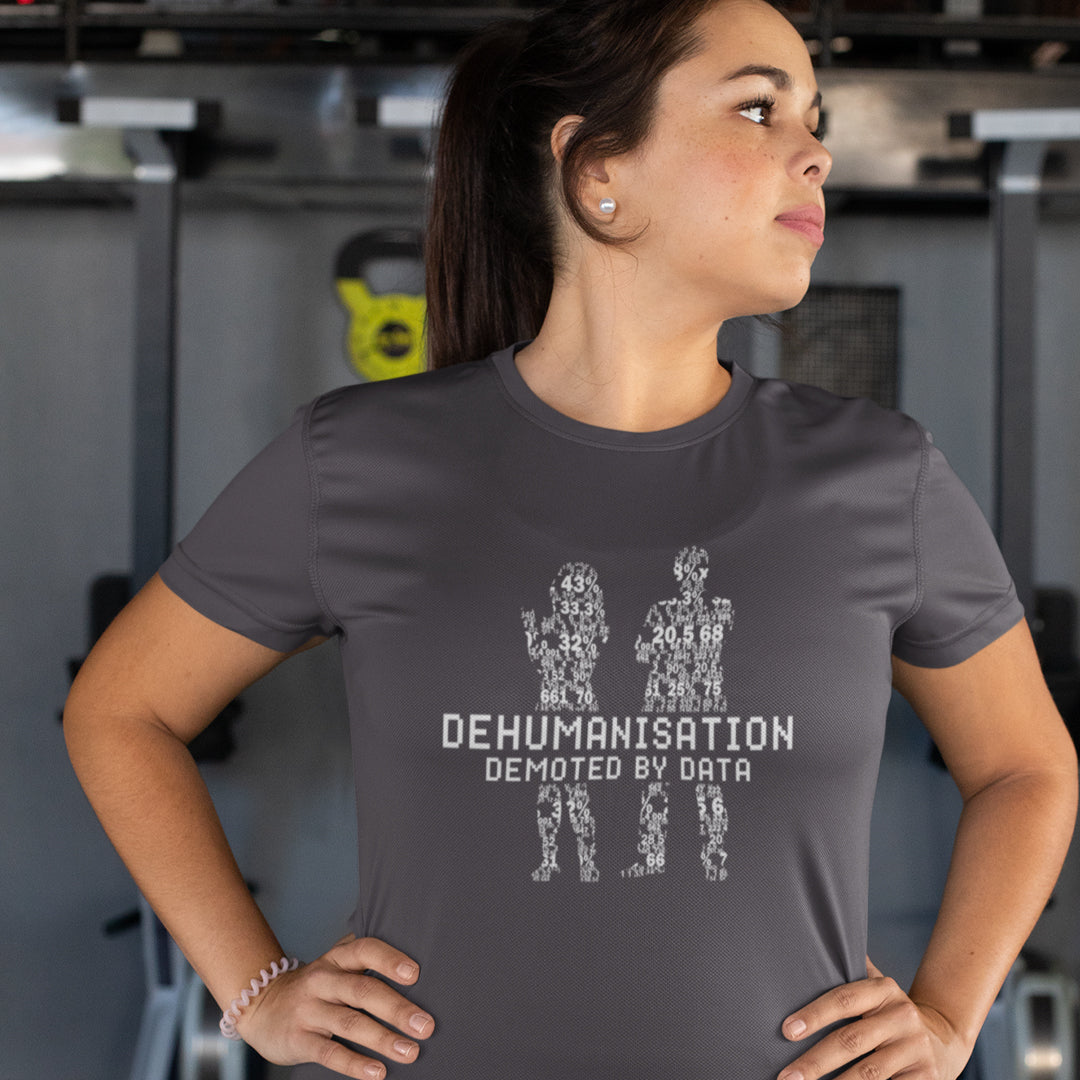 Person wearing a dark grey t-shirt with text and graphics, standing in an indoor setting. This broken society t shirt depicts the dehumanisation of the species by analysis and data collection. The more we view each other as statistics and numbers the further we move away from compassion and empathy. This design highlights the dark side of progression. Made from 100% organic ring-spun cotton, this dystopian t shirt is unisex, high-quality, super comfy, and best of all, eco-friendly.