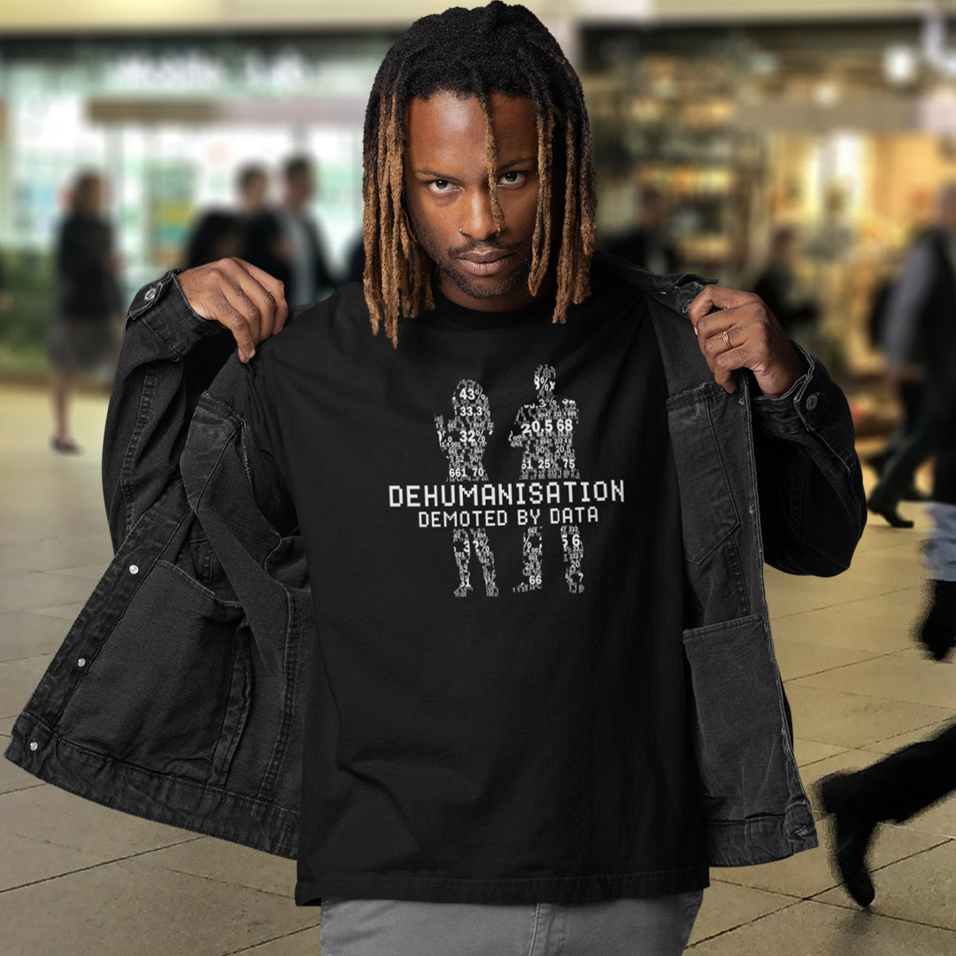 Man wearing a black t-shirt with text and graphics, standing in a public area. This broken society t shirt depicts the dehumanisation of the species by analysis and data collection. The more we view each other as statistics and numbers the further we move away from compassion and empathy. This design highlights the dark side of progression. Made from 100% organic ring-spun cotton, this dystopian t shirt is unisex, high-quality, super comfy, and best of all, eco-friendly.