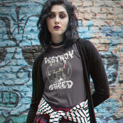 A woman with dark hair stands in front of a graffiti-covered brick wall, wearing a dark gray graphic t-shirt with the words 'DESTRUCTION GREED' and a black cardigan, with a red, black, and white striped shirt tied around her waist.