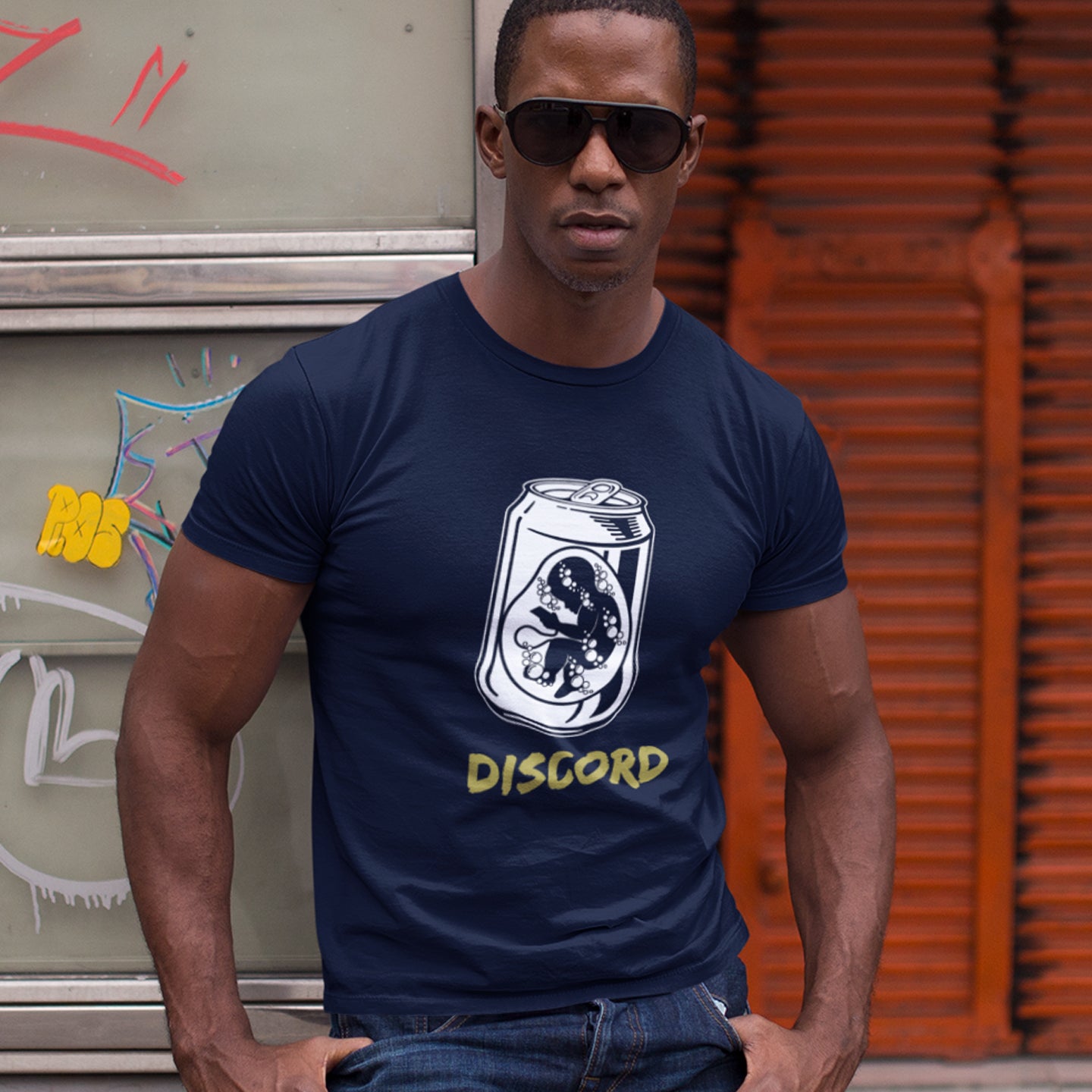 Man wearing a French navy blue t-shirt with a Discord logo in front of a graffiti-covered wall. A stencil graffiti t shirt suggesting a discord between modern generations and nature. A street art t shirt testament to the soda pop generation. Brought up on energy drinks and born with a Wi-Fi connection. Made from 100% organic ring-spun cotton, this urban art t shirt is unisex, high-quality, super comfy, and best of all, eco-friendly.