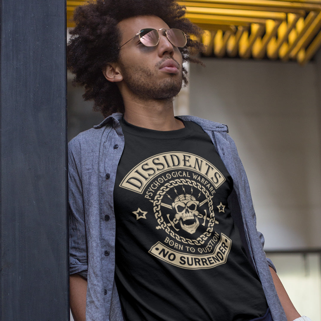 Man wearing a black t-shirt with 'Dissidents' design, leaning against a wall. An anti government t shirt suggesting we are living in a psychological war. Designed in a motorcycle club style, this dissident t shirt is for those among us that feel they are fighting for their freedom to think independently and to make their own choices. Made from 100% organic ring-spun cotton, this non conformist t shirt is unisex, high-quality, super comfy, and best of all, eco-friendly.