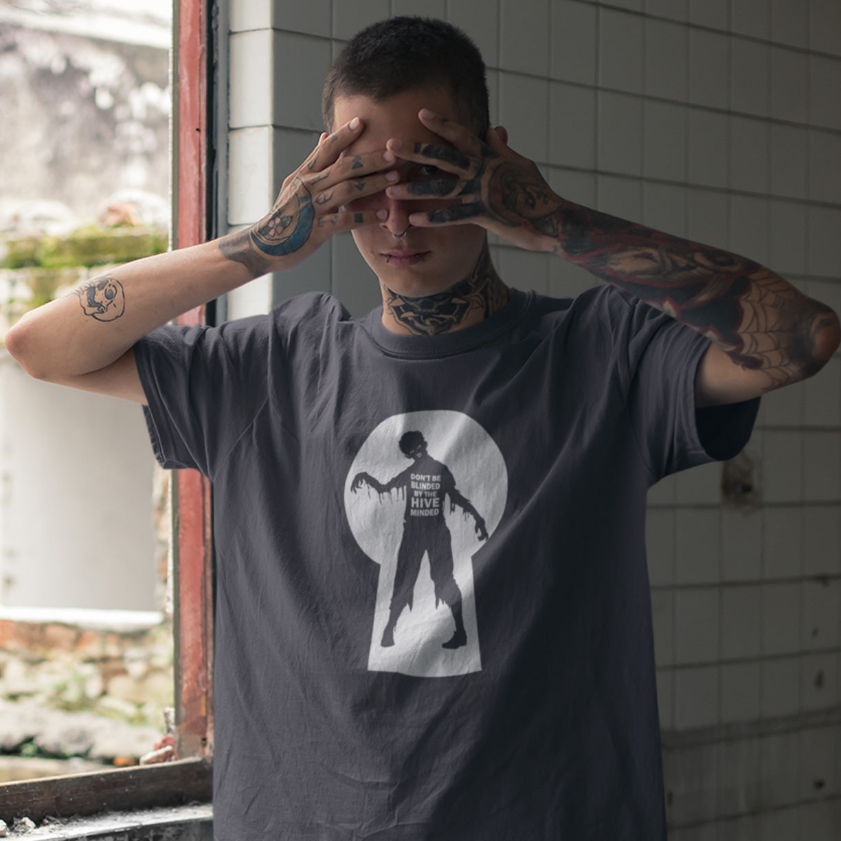 A tattooed man wearing a dark gray t-shirt with a white keyhole graphic containing a zombie silhouette.