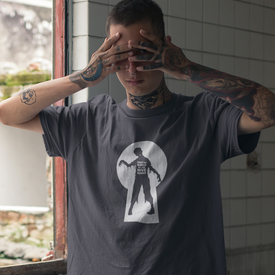 A tattooed man wearing an anthracite grey  t-shirt with a zombie through a key hole design with "DON'T BE BLINDED BY THE HIVE MINDED" text.