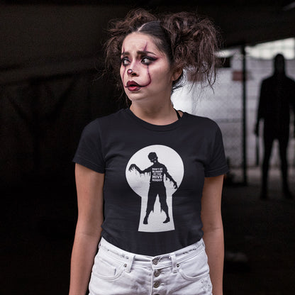 A woman with dramatic zombie makeup and messy hair wears a black graphic t-shirt featuring a white keyhole design with a zombie silhouette.