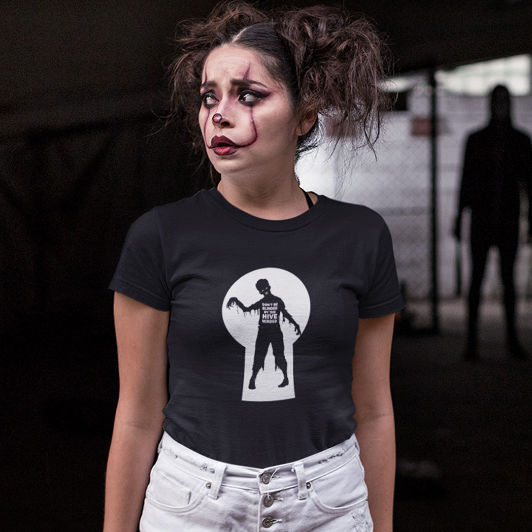 A woman with clown makeup, looking worried with a man standing in the shadows, wearing a black  t-shirt with a zombie through a key hole design with "DON'T BE BLINDED BY THE HIVE MINDED" text.