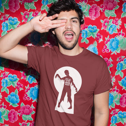 A man wearing a brown t-shirt with a zombie graphic, posing with his hand over his eye in front of a red floral backdrop.