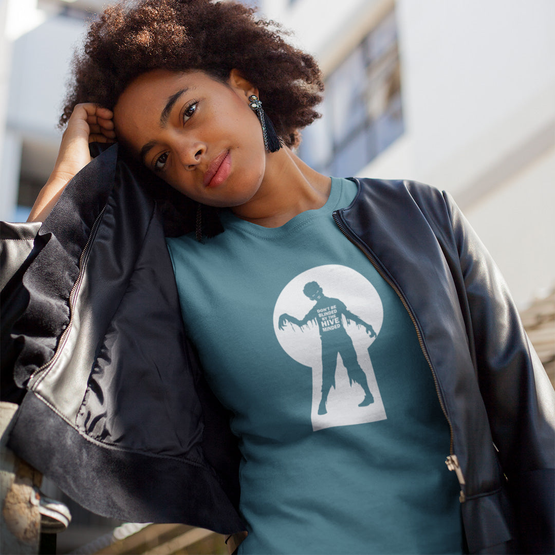 A woman wearing a stargazer blue graphic  t-shirt with a zombie through a key hole design with "DON'T BE BLINDED BY THE HIVE MINDED" text.