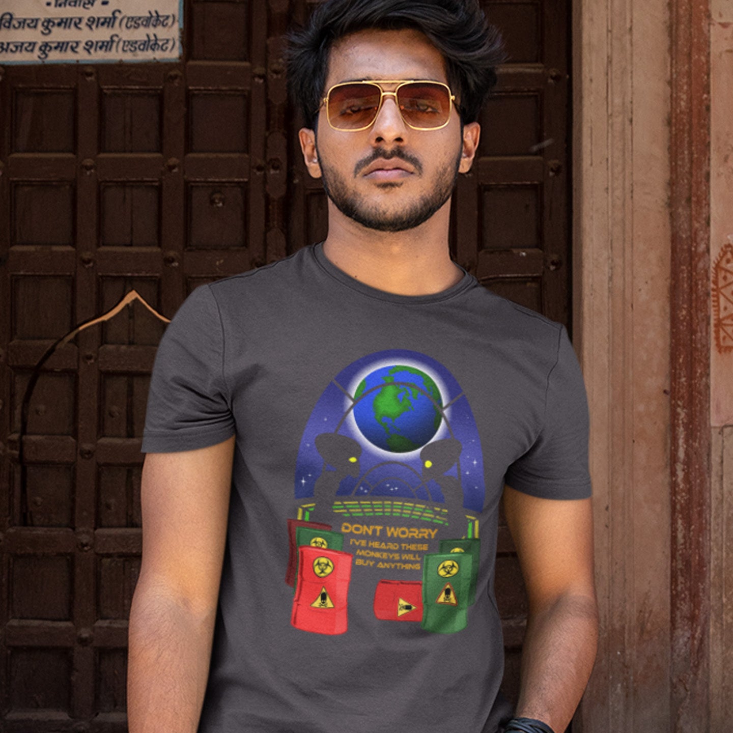 Man wearing an anthracite t-shirt with a colourful graphic design in front of a wooden door. A funny alien t shirt design showing a humorous view of how aliens must see us. It's universally acknowledged that humans have an obsession with shopping and buying things they don't need. Made from 100% organic ring-spun cotton, these cool sci fi t shirts are unisex, high-quality, super comfy, and best of all, eco-friendly.