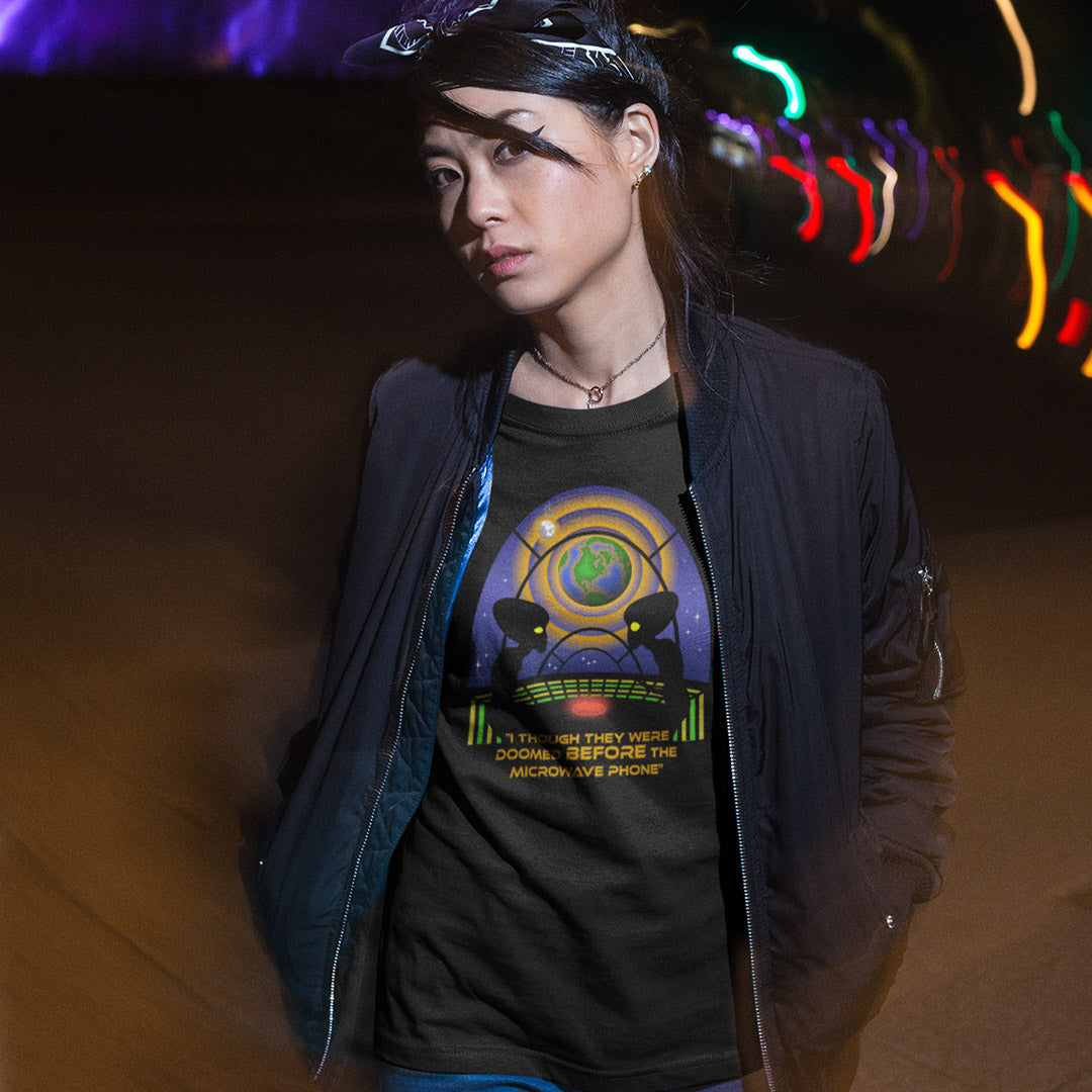 Woman standing outdoors at night wearing a black funny alien t shirt. A funny alien t shirt satirically exposing the dangers of microwaves. We probably seem quite masochistic from an outsiders point of view and the aliens must wonder what we are doing in the name of progression. A global warming t shirt design for alien fans. Made from 100% organic ring-spun cotton, this cool sci fi t shirt is unisex, high-quality, super comfy, and best of all, eco-friendly.