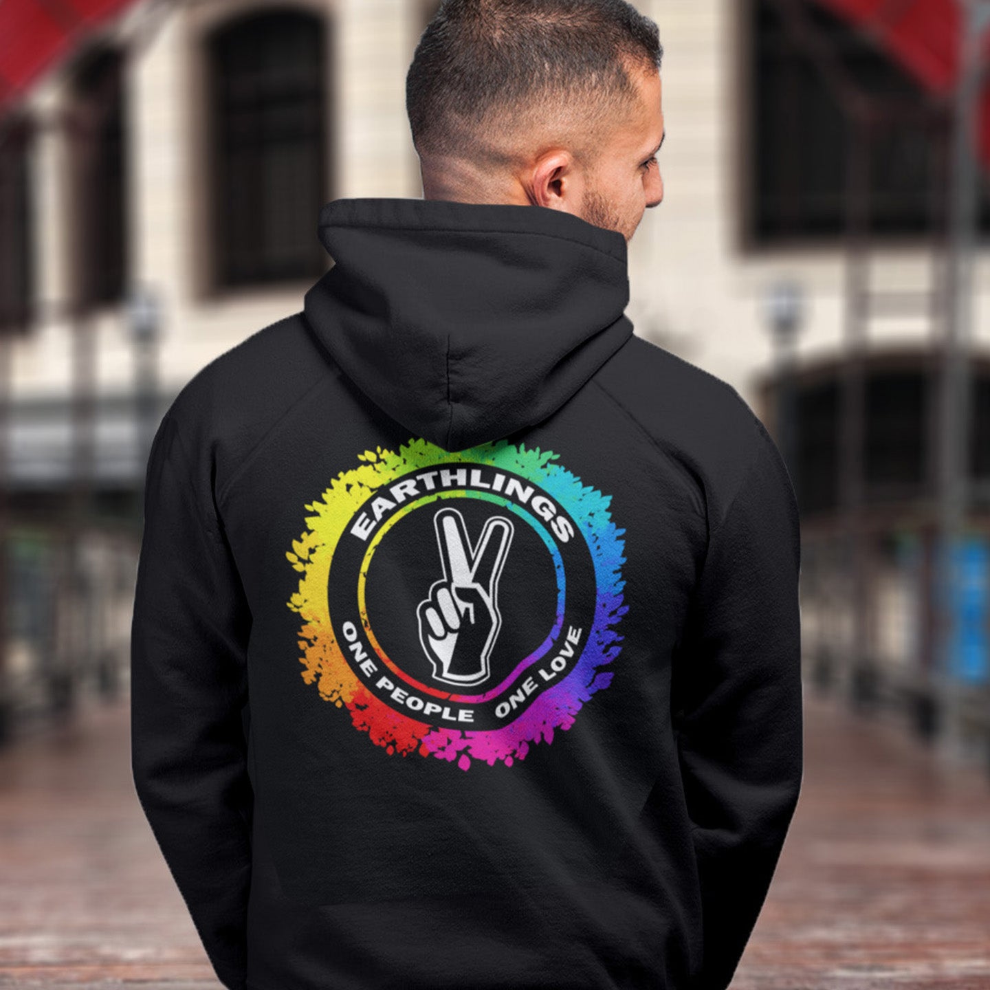 Person wearing a black hoodie with a colourful design on the back, featuring text and a peace symbol. This ant-prejudice hoodie is LGTBQ+ friendly and anti-racism. We are all Earthlings and can live in peace and harmony if we put aside our prejudice and fear. This original design promotes social awareness and unity. Comfortable and practical. It's extra soft and has a convenient front pouch pocket. Made from organic cotton and recycled polyester, this anti prejudice hoodie is a great eco-friendly choice.