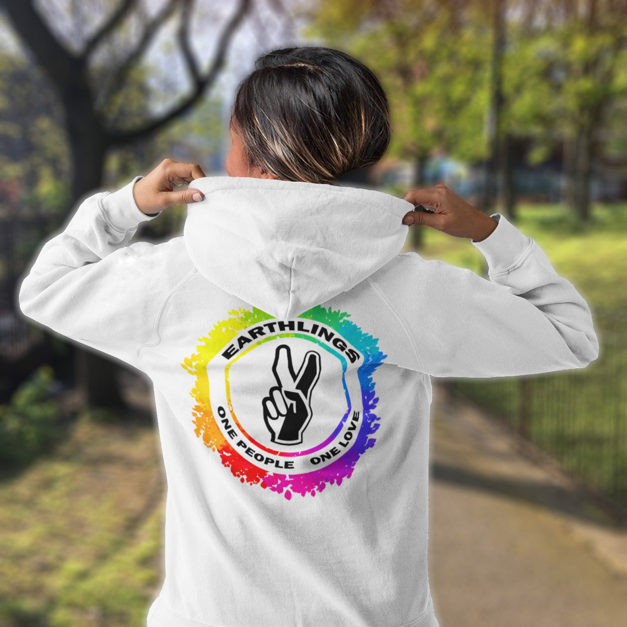 Person wearing a white hoodie with a colourful logo and text in an outdoor setting. This ant-prejudice hoodie is LGTBQ+ friendly and anti-racism. We are all Earthlings and can live in peace and harmony if we put aside our prejudice and fear. This original design promotes social awareness and unity. Comfortable and practical. It's extra soft and has a convenient front pouch pocket. Made from organic cotton and recycled polyester, this anti prejudice hoodie is a great eco-friendly choice.