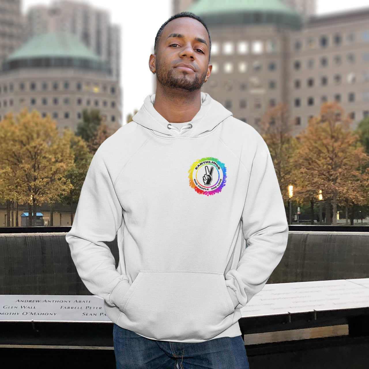 Man wearing a white hoodie with a colourful logo in an urban setting. This ant-prejudice hoodie is LGTBQ+ friendly and anti-racism. We are all Earthlings and can live in peace and harmony if we put aside our prejudice and fear. This original design promotes social awareness and unity. Comfortable and practical. It's extra soft and has a convenient front pouch pocket. Made from organic cotton and recycled polyester, this anti prejudice hoodie is a great eco-friendly choice.