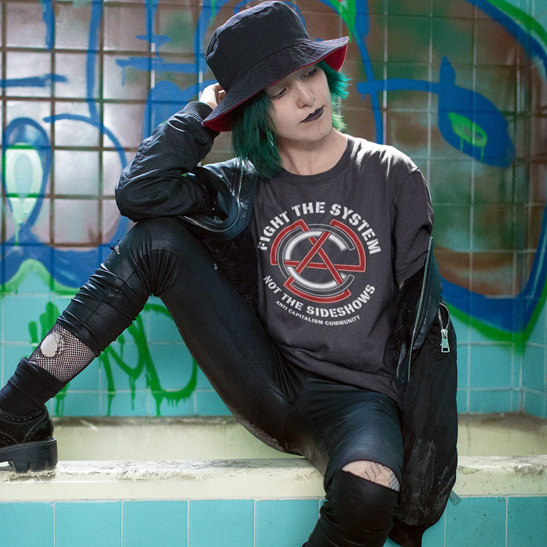 Person wearing a dark t shirt t, sitting against a graffiti-covered wall. This anti establishment t shirt speaks out against capitalism and warns not to be side tracked by the individual problems created by the overall system. Capitalism is responsible for so many of societies problems, do not accept it. Join our community and be proud to wear the shirt. Made from 100% organic ring-spun cotton, this anti capitalist t shirt is unisex, high-quality, super comfy, and best of all, eco-friendly.
