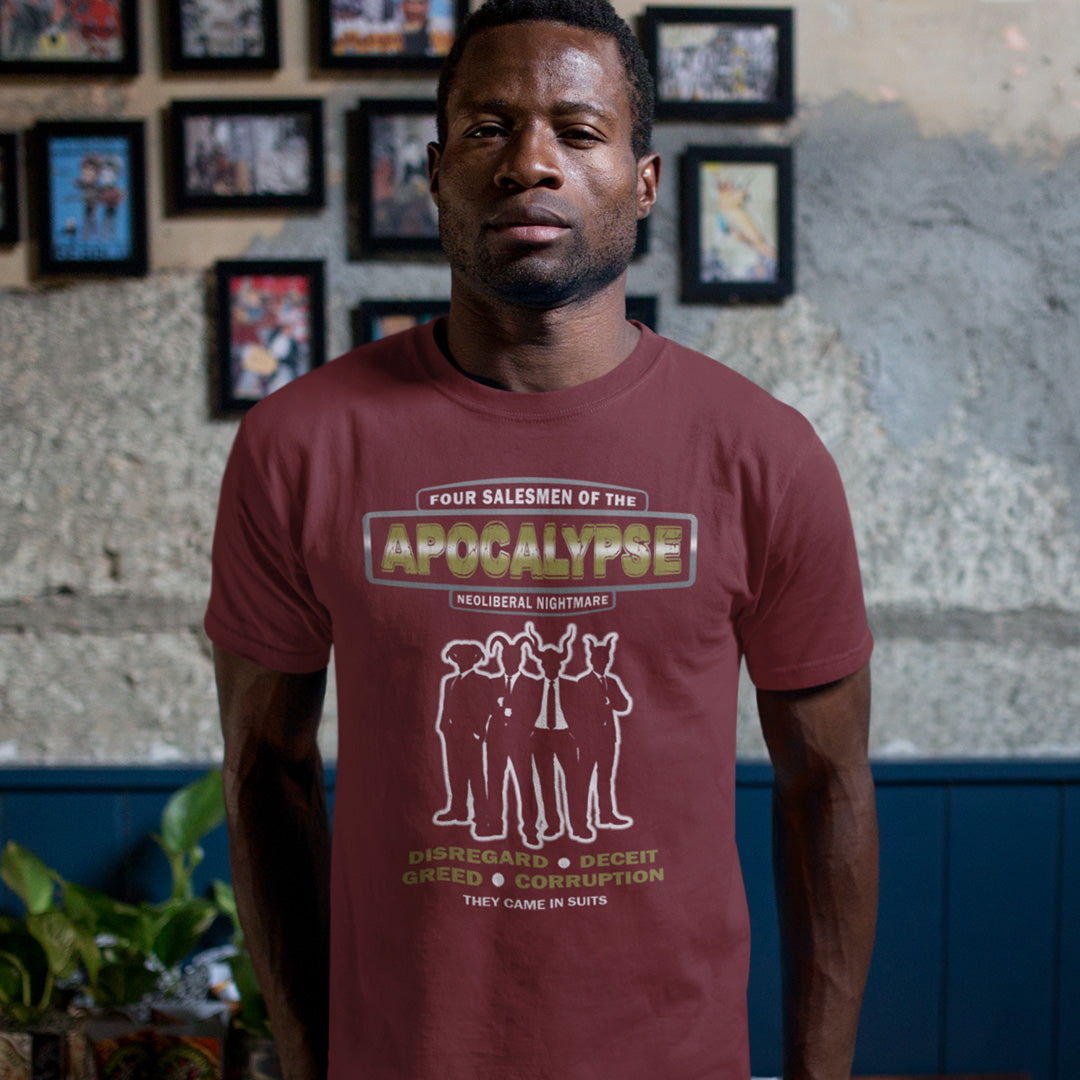 Man wearing a red t-shirt with graphic design and text, standing in front of a wall with framed pictures. An anti capitalism t shirt with a biblical undertone. A satirical design looking at how neoliberalism and it's hidden inequalities could bring on the downfall of civilised society and the form it will take. Made from 100% organic ring-spun cotton, this non conformist t shirt is a total must-have. It's high-quality, super comfy, and best of all, eco-friendly.
