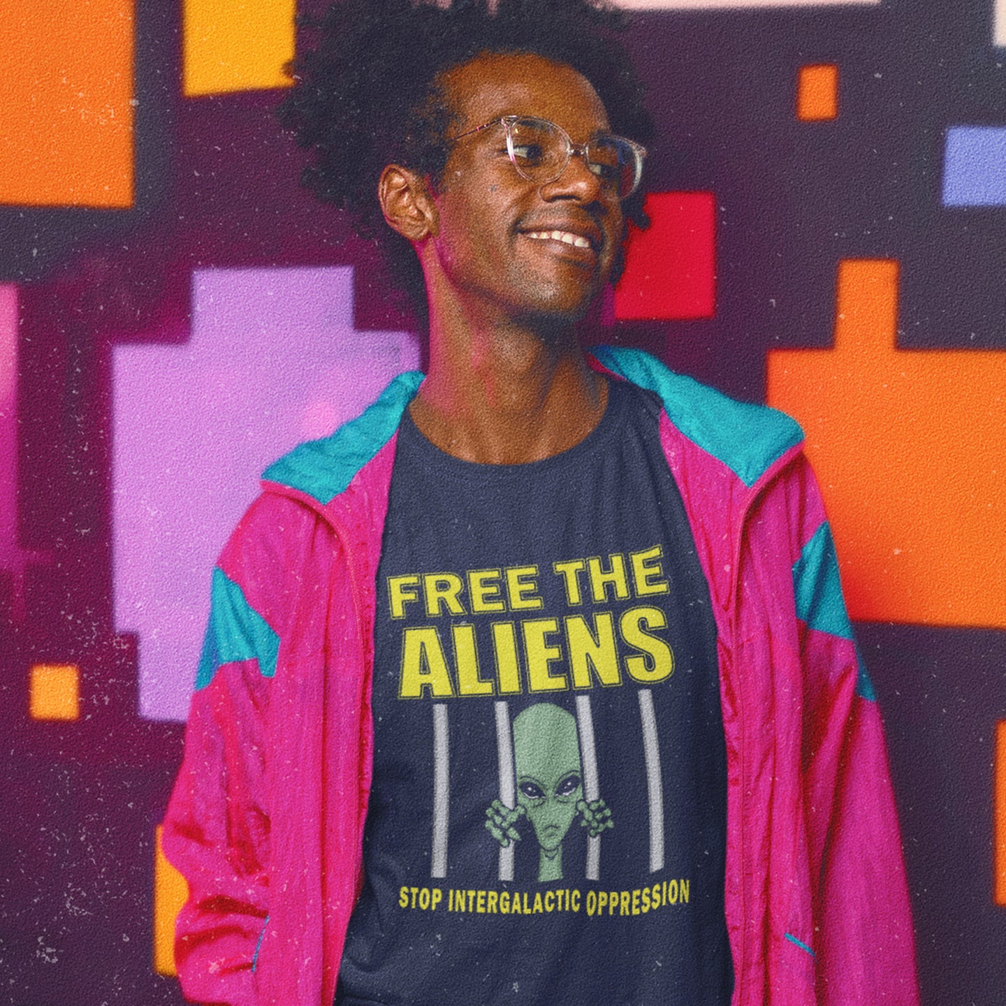 Person wearing a shirt with 'Free the Aliens' text and graphic, standing in front of a colourful geometric-patterned wall. This funny alien conspiracy theory t-shirt alludes to there being more than just UFO crashes that we are not being told about. With all these alien sightings they must detaining them somewhere ! Made from 100% organic ring-spun cotton, this conspiracy theory t-shirt is unisex, high-quality, super comfy, and best of all, eco-friendly.