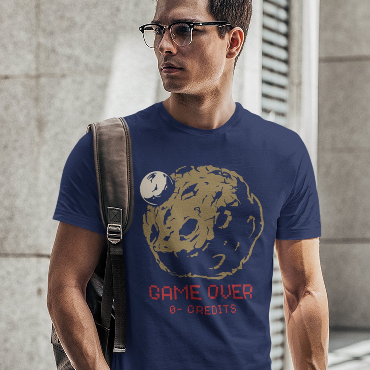 Man wearing a French navy t-shirt with a graphic design and text, standing against a concrete wall. A save the earth t shirt design suggesting we are not taking our environmental issues seriously enough, and are treating it all like a game. The problem is that when this game ends, it ends. Planet and environmental concern for gamers and everybody else. Made from 100% organic ring-spun cotton, this save the earth t shirt is unisex, high-quality, super comfy, and best of all, eco-friendly.