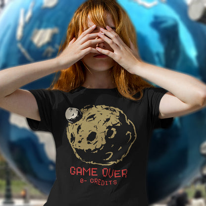 Person wearing a black t-shirt with a graphic design and text, covering their face with their hands. A save the earth t shirt design suggesting we are not taking our environmental issues seriously enough, and are treating it all like a game. The problem is that when this game ends, it ends. Planet and environmental concern for gamers and everybody else. Made from 100% organic ring-spun cotton, this save the earth t shirt is unisex, high-quality, super comfy, and best of all, eco-friendly.