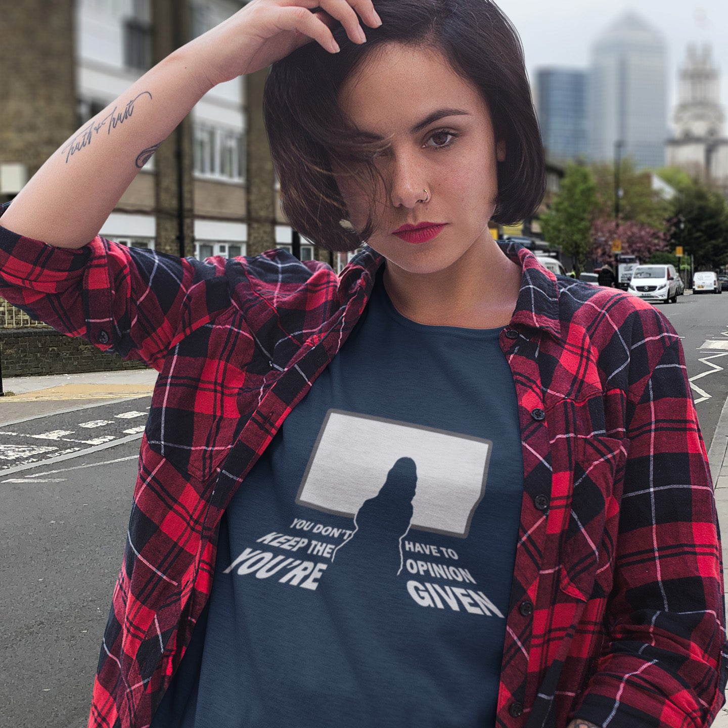 Woman wearing a French navy  blue t-shirt with text and a red plaid shirt outdoors. A non conformist t shirt design to promote self awareness. In a age of external influence. especially from mass media, lets not forget that you still own the right to investigate and form your own opinion. A design to promote independent thought and the need to think outside the box. Made from 100% organic ring-spun cotton, this self worth t shirt is unisex, high quality, super comfy, and best of all, eco-friendly.
