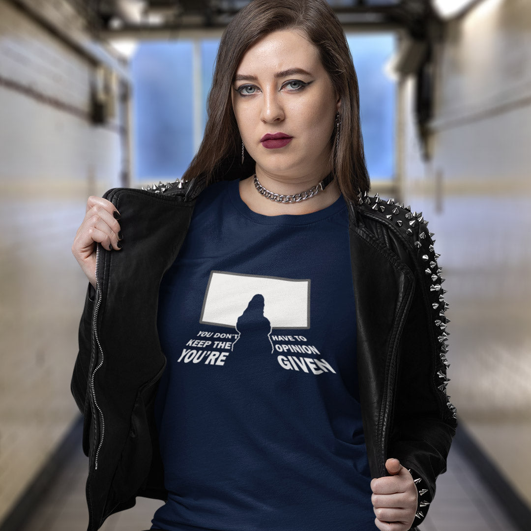 A woman wearing a navy blue graphic t-shirt and a black studded leather jacket, standing in a blurred indoor hallway.