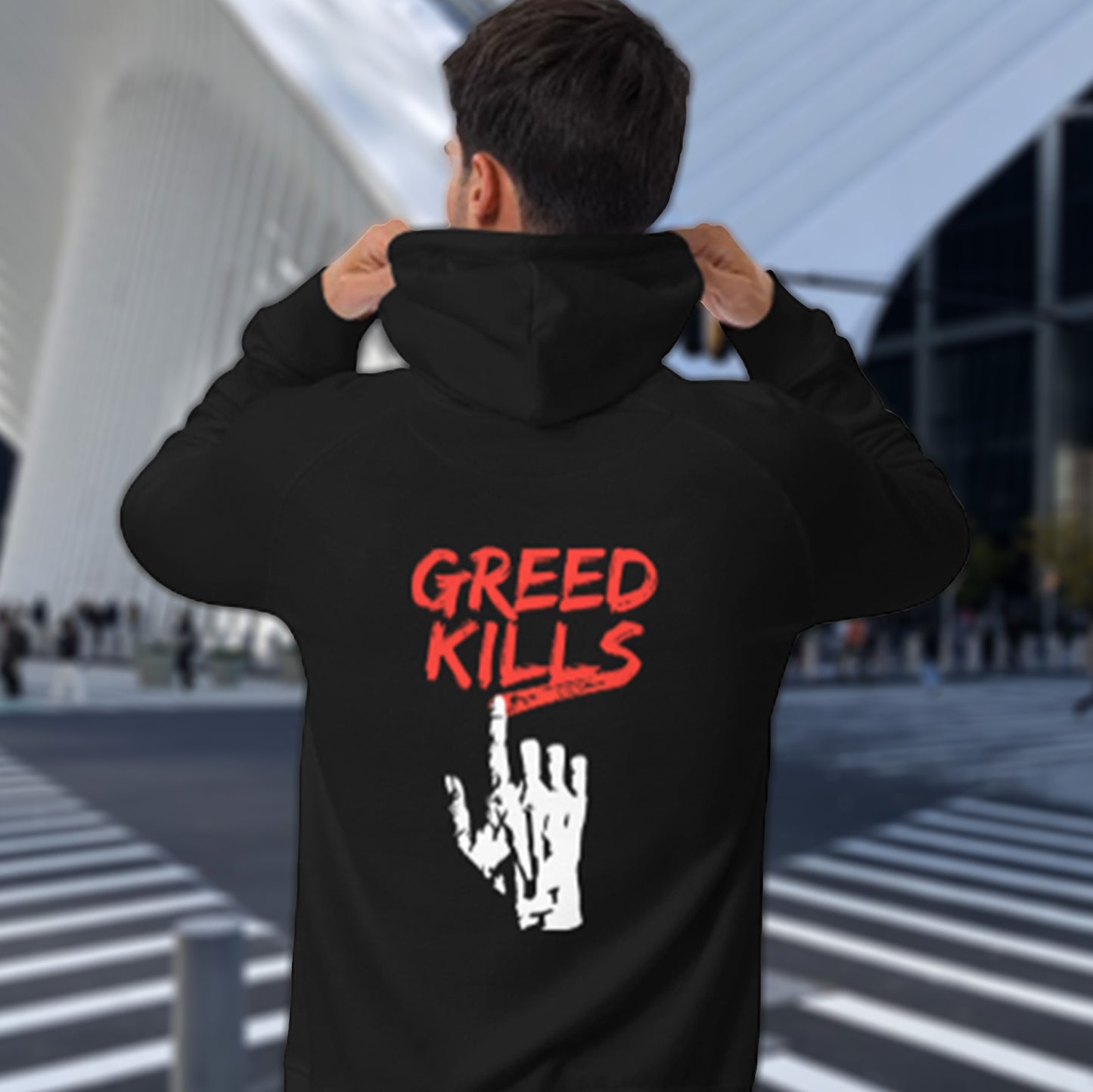 Person wearing a black hoodie with 'GREED KILLS' text, standing in an outdoor modern architectural setting. An anti-capitalism t-shirt focusing on greed. It's the slow-creeping, strong-holding virus that has been with us since the beginning of time, yet we still can't find a cure. Comfortable and practical. It's extra soft and has a convenient front pouch pocket. Made from organic cotton and recycled polyester, this social awareness hoodie is a great eco-friendly choice for the anti-capitalist. 