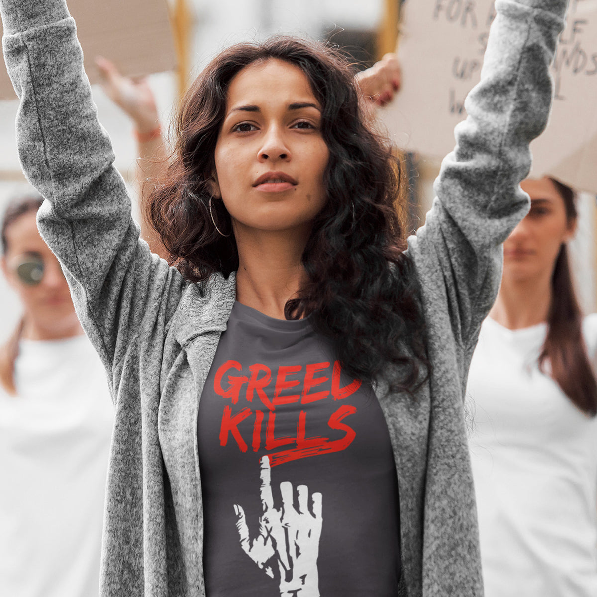 A woman holding up a placard at a rally wearing an anthracite  crew neck t-shirt with a hand writing "GREED KILLS" in blood red. 