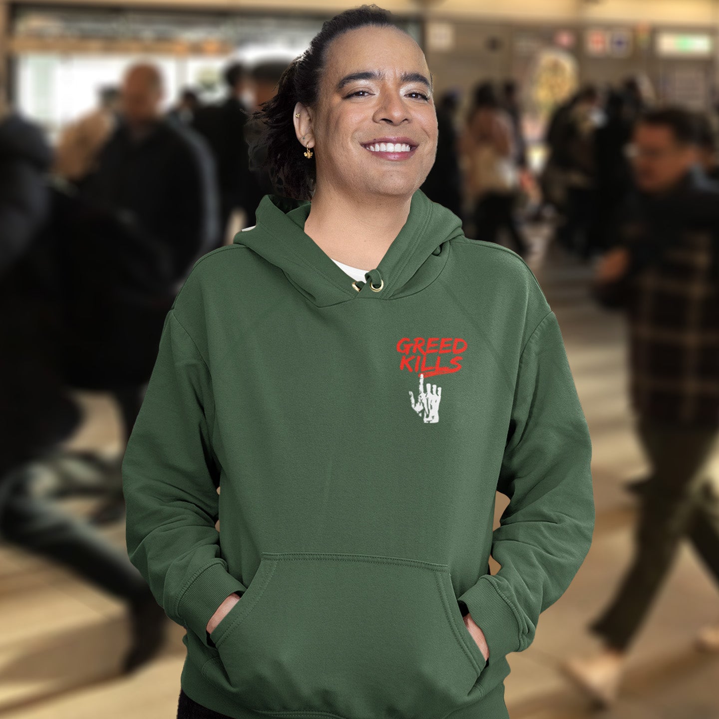 Person wearing a bottle green hoodie with text in an urban setting. An anti-capitalism hoodie design focusing on greed. It's the slow-creeping, strong-holding virus that has been with us since the beginning of time, yet we still can't find a cure. Comfortable and practical. It's extra soft and has a convenient front pouch pocket. Made from organic cotton and recycled polyester, this non conformist hoodie is a great eco-friendly choice for the anti-capitalist.