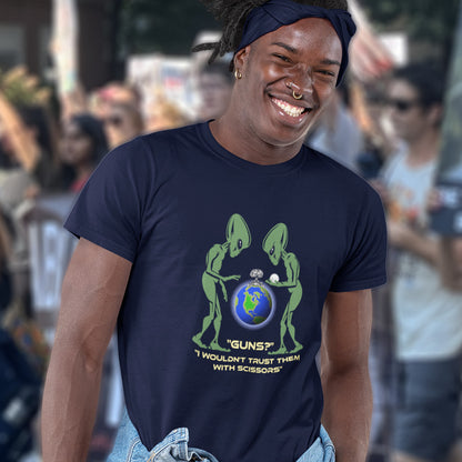 Person wearing a navy blue t-shirt with a graphic design and text, standing in a crowd. This funny alien t shirt highlights our over use of weaponry. With our lust for guns we must look out of control from an alien view point. No wonder they don't openly reveal themselves to us. Made from 100% organic ring-spun cotton, this counter culture t shirt is unisex, high-quality, super comfy, and best of all, eco-friendly.