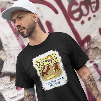 A man wearing a black graphic t-shirt with a retro-style illustration and the text 'I JUST DON'T FIT IN ANYWHERE' on the front, paired with a white baseball cap, posed against a graffiti-covered wall.