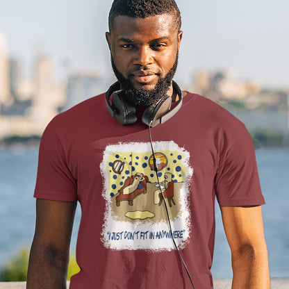 Man wearing a burgundy t-shirt with a graphic design and text, standing outdoors with a blurred cityscape in the background. A funny cartoon t-shirt for all you 'square pegs in round holes' out there. You are not alone. This unique design is ideal for anyone who thinks outside the box. Made from 100% organic ring-spun cotton, this witty cartoon t-shirt is unisex, high-quality, super comfy, and best of all, eco-friendly.