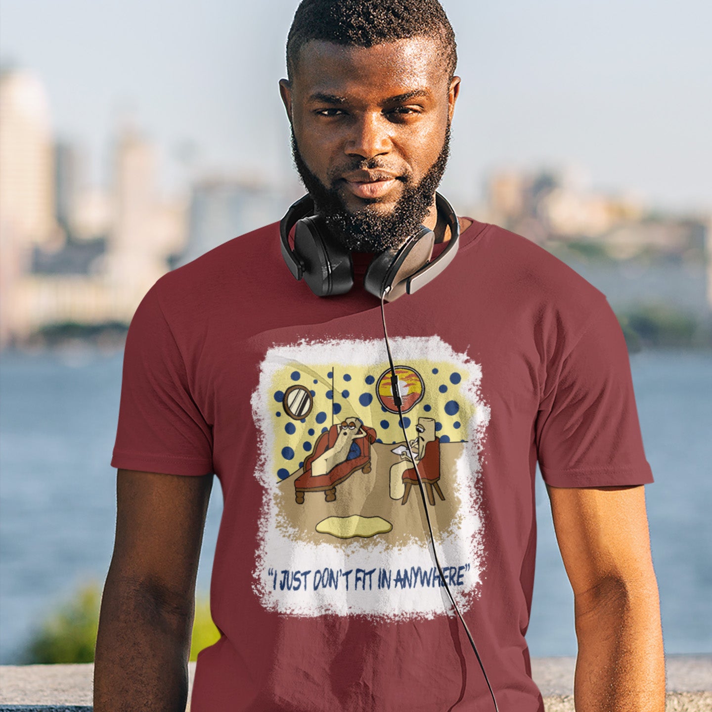 Man wearing a burgundy t-shirt with a graphic design and text, standing by a waterfront with a cityscape in the background. A funny non conformist t shirt for all you 'square pegs in round holes' out there. You are not alone. This unique design is ideal for anyone who thinks outside the box. Made from 100% organic ring-spun cotton, this sarcastic slogan t shirt is unisex, high-quality, super comfy, and best of all, eco-friendly.
