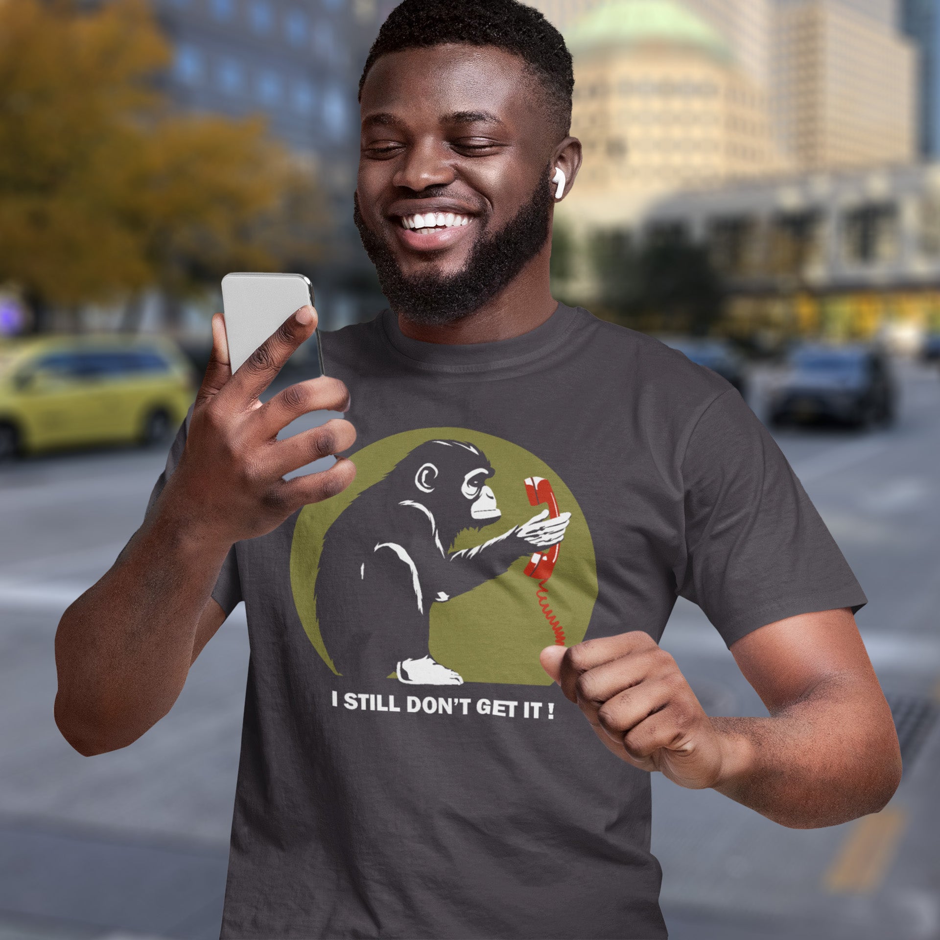 Man wearing a t-shirt with a monkey holding a phone graphic and text, standing on a city street. This anti smart phone abuse t-shirt design highlights the human obsession with smart phones and how strange it must look to an ape. An outsiders view of a world glued to mobile phones. Made from 100% organic ring-spun cotton, this anti mobile phone abuse t-shirt is unisex, high-quality, super comfy, and best of all, eco-friendly.
