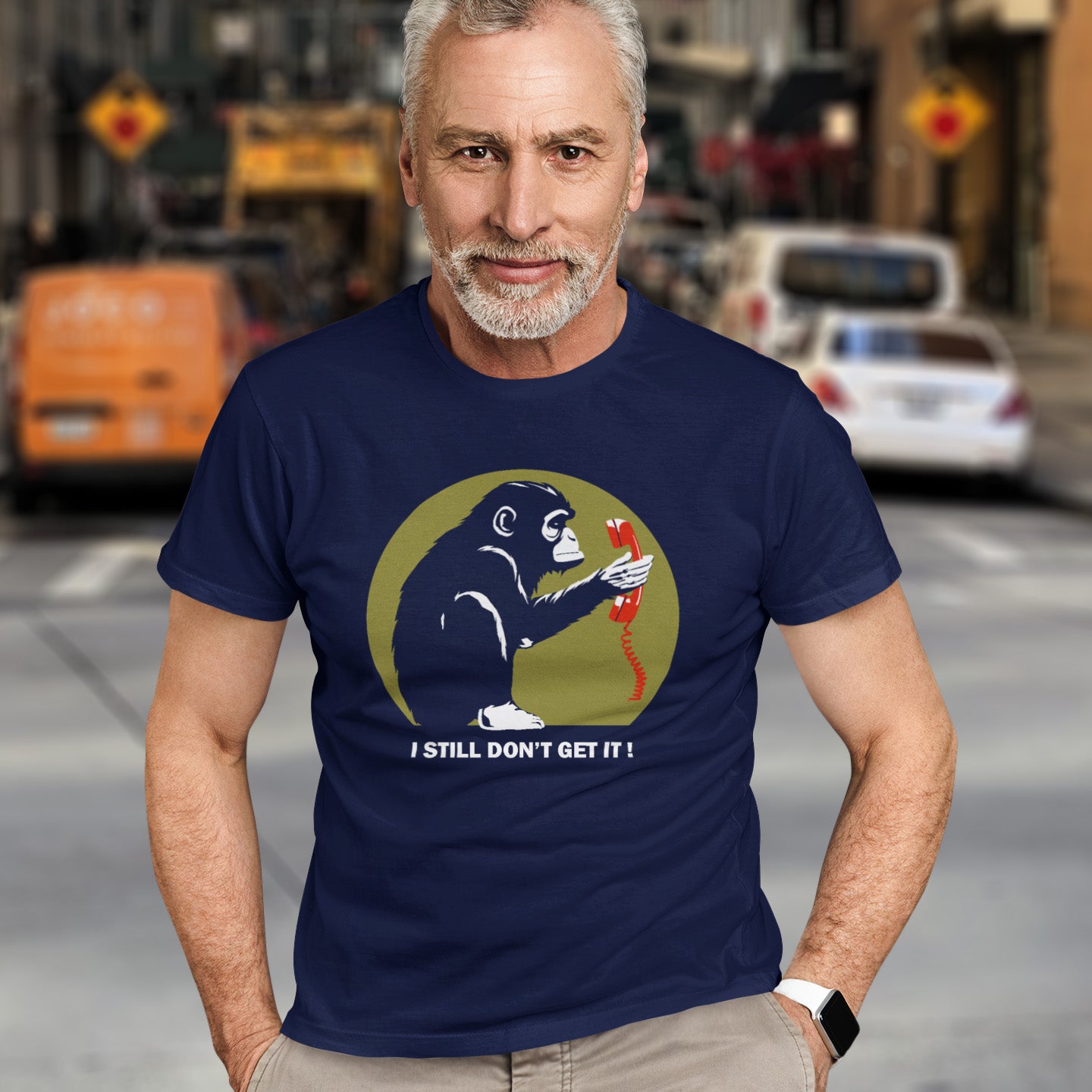 Man wearing a French navy blue t-shirt with a graphic design and text, standing on a street. This satirical Banksy style stencil art t-shirt design highlights the human obsession with smart phones and how strange it must look to an ape. An outsiders view of a world glued to mobile phones. Made from 100% organic ring-spun cotton, this street art social awareness t-shirt is unisex, high-quality, super comfy, and best of all, eco-friendly.