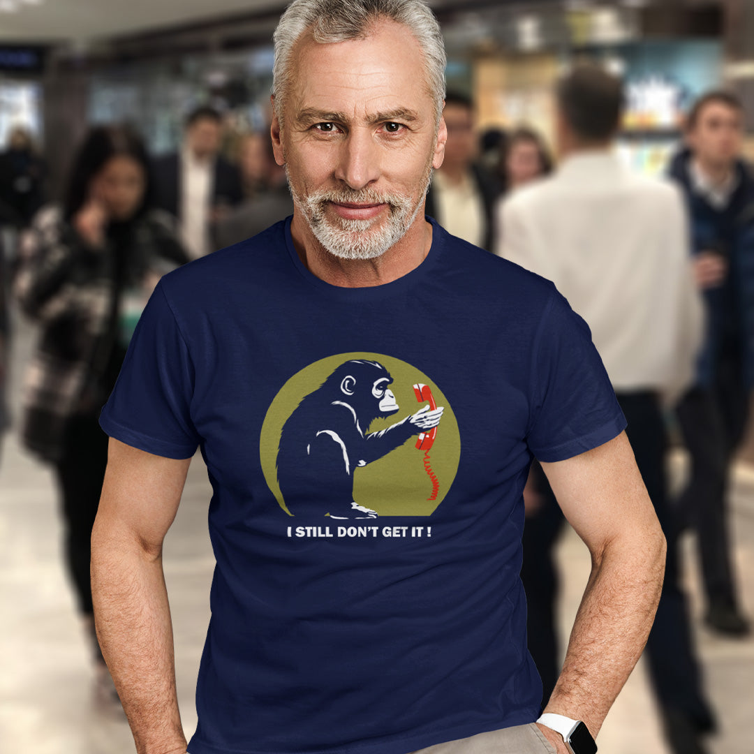 A man in a shopping centre, wearing a French navy blue t-shirt with a design of a monkey staring at an old style telephone receiver with text underneath saying "I STILL DON'T GET IT".