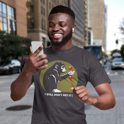 Man wearing a t-shirt with a graphic design of a monkey holding a phone and text 'I STILL DON'T GET IT!' on a city street. This satirical Banksy style stencil art t-shirt design highlights the human obsession with smart phones and how strange it must look to an ape. An outsiders view of a world glued to mobile phones. Made from 100% organic ring-spun cotton, this street art social awareness t-shirt is unisex, high-quality, super comfy, and best of all, eco-friendly.