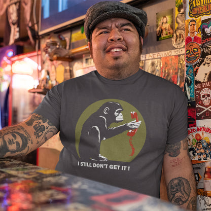 Man wearing a t-shirt with a graphic design of a monkey holding a phone and text 'I STILL DON'T GET IT!' in a tattoo parlour. This anti smart phone abuse t-shirt design highlights the human obsession with smart phones and how strange it must look to an ape. An outsiders view of a world glued to mobile phones. Made from 100% organic ring-spun cotton, this anti mobile phone abuse t-shirt is unisex, high-quality, super comfy, and best of all, eco-friendly.