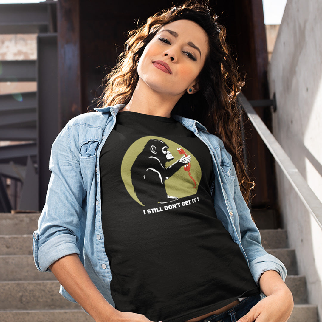 A woman wearing a black graphic t-shirt with a design of a monkey staring at an old style telephone receiver with text underneath saying "I STILL DON'T GET IT".