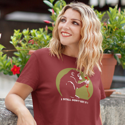 A blonde woman, smiling and wearing a burgundy t-shirt with a design of a monkey staring at an old style telephone receiver with text underneath saying "I STILL DON'T GET IT".
