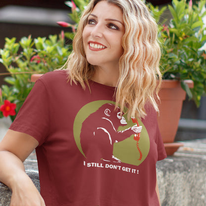 Woman wearing a burgundy t-shirt with a graphic design and text, standing outdoors. This anti smart phone abuse t-shirt design highlights the human obsession with smart phones and how strange it must look to an ape. An outsiders view of a world glued to mobile phones. Made from 100% organic ring-spun cotton, this anti mobile phone abuse t-shirt is unisex, high-quality, super comfy, and best of all, eco-friendly.
