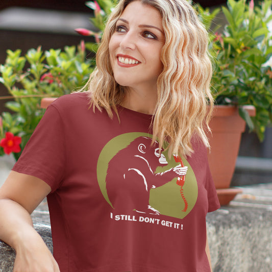 Woman wearing a burgundy t-shirt with a graphic design and text, standing outdoors. This anti smart phone abuse t-shirt design highlights the human obsession with smart phones and how strange it must look to an ape. An outsiders view of a world glued to mobile phones. Made from 100% organic ring-spun cotton, this anti mobile phone abuse t-shirt is unisex, high-quality, super comfy, and best of all, eco-friendly.