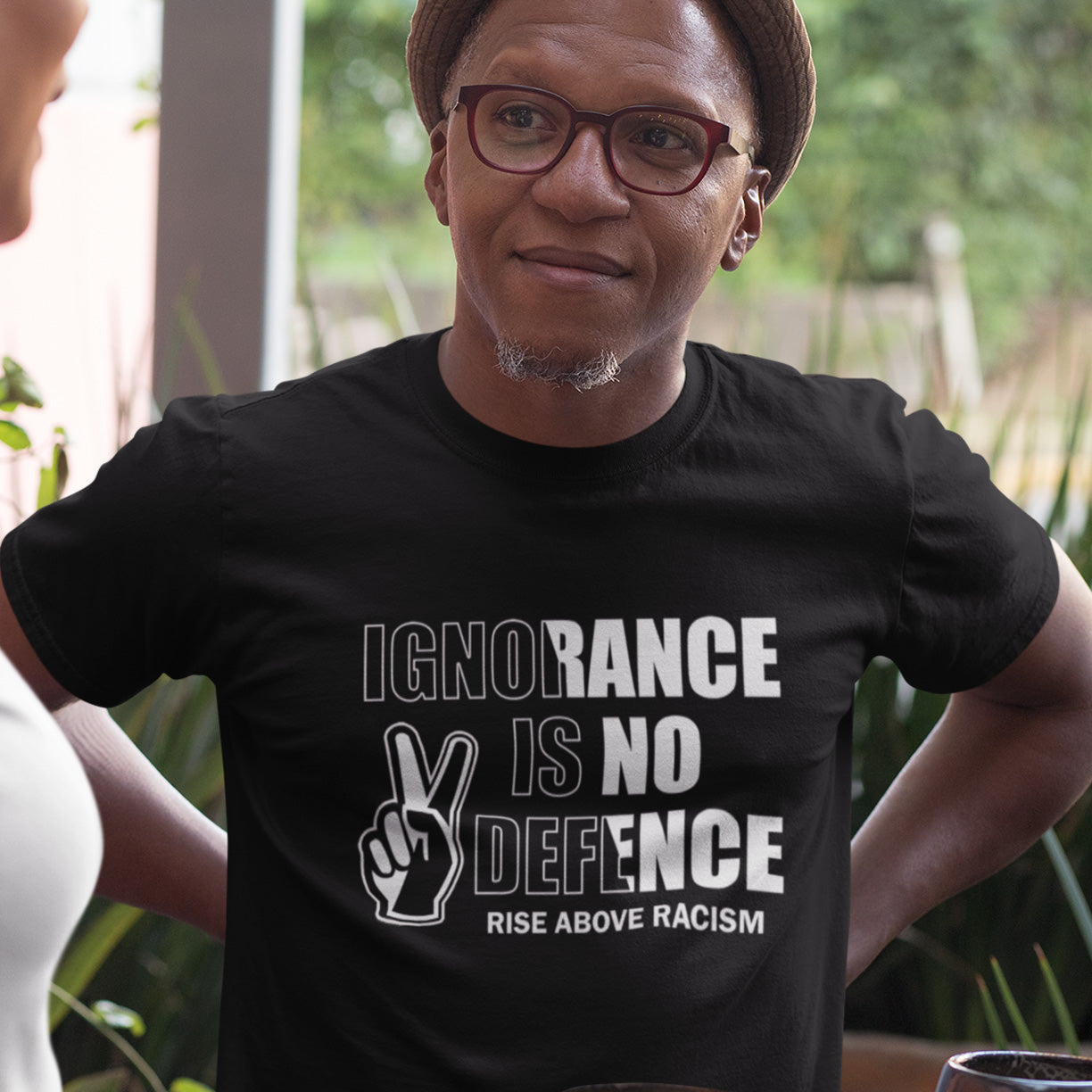 Person wearing a black t-shirt with 'Ignorance is No Defence' text and graphic. An anti-racist t-shirt to remind people that ignorance is no defence against prejudice. This unique racial equality t-shirt design promotes understanding and brotherhood to achieve peace in the world. Made from 100% organic ring-spun cotton, this anti racism t-shirt is unisex, high-quality, super comfy, and best of all, eco-friendly.