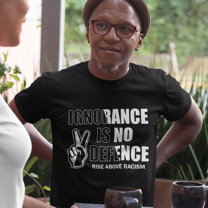 A man wearing a black graphic t-shirt with the text 'IGNORANCE IS NO DEFENCE RISE ABOVE RACISM' and a peace sign hand graphic, standing in a lifestyle setting.